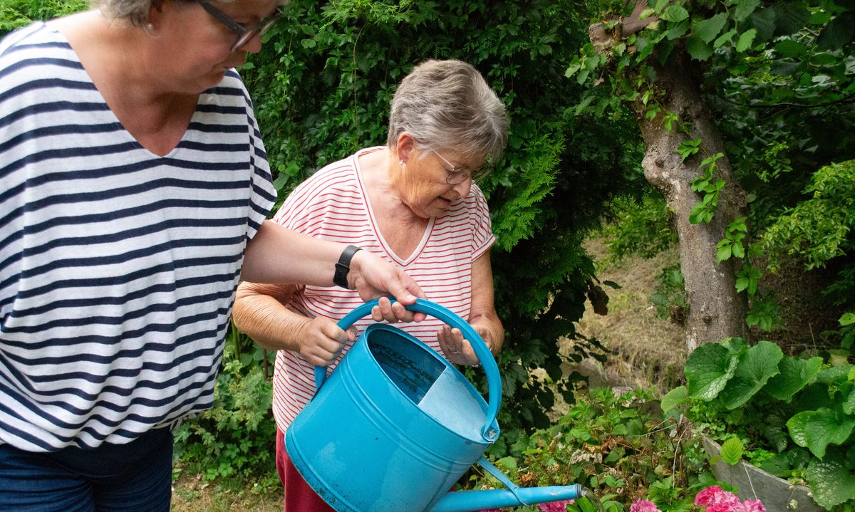 Brigitte Keller giesst gemeinsam mit einer Kundin Blumen im Garten